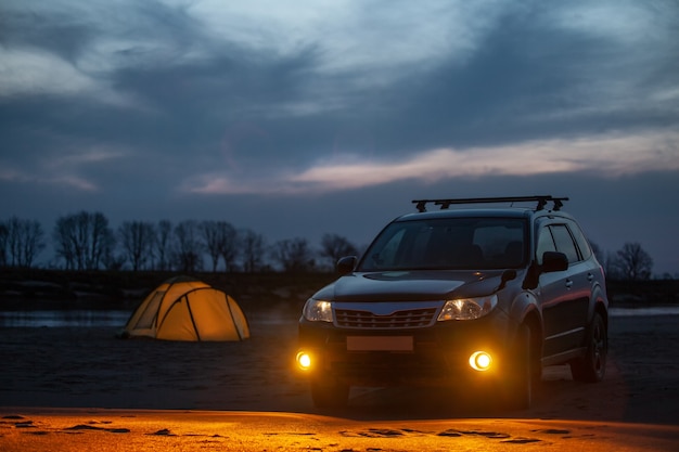 Camping au coucher du soleil sur une berge de sable. Crossover noir avec feux de brouillard allumés