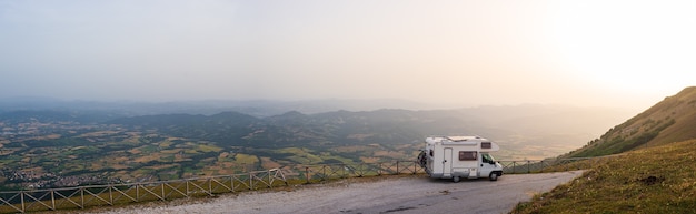 Camping-car au bord de la route dans un paysage magnifique. Ciel dramatique au coucher du soleil, nuages pittoresques au-dessus des hauts plateaux uniques et de la chaîne de collines en Italie, concept alternatif de vacances vanlife.