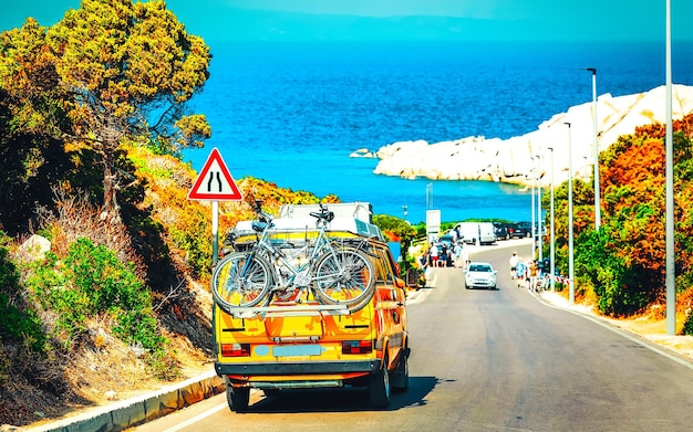 Camping-car avec vélos sur route à Capo Testa à Santa Teresa Gallura en mer Méditerranée sur l'île de Sardaigne, Italie l'été. Camping-car caravane en vacances sur l'autoroute. Minivan rv sur autoroute. Technique mixte.