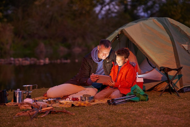 Le camping n'est pas toujours à la dure Photo d'un père et de son fils regardant un film sur une tablette numérique en camping