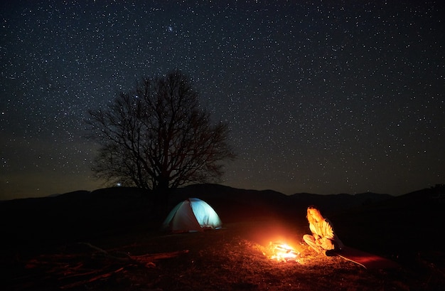 Camping de nuit. Randonneur au repos près d'un feu de camp sous un ciel étoilé