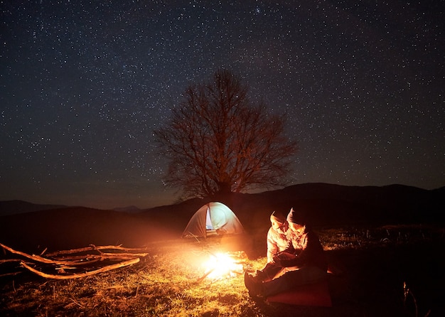 Camping de nuit. Les randonneurs se reposant près d'un feu de camp sous un ciel étoilé