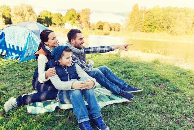 camping, tourisme, randonnée et concept de personnes - famille heureuse sur une tente au camping pointant du doigt quelque chose