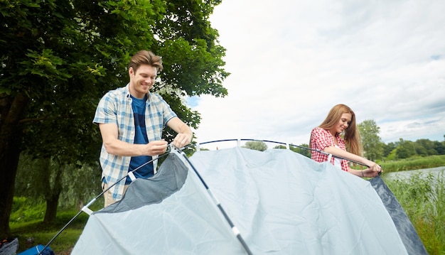 camping, voyage, tourisme, randonnée et concept de personnes - couple heureux installant une tente à l'extérieur