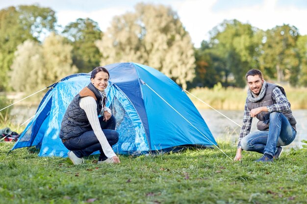 camping, voyage, tourisme, randonnée et concept de personnes - couple heureux installant une tente à l'extérieur