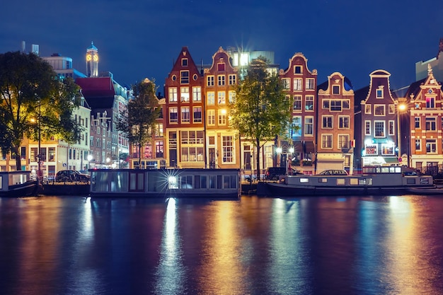 Photo canal d'amsterdam amstel avec des maisons hollandaises typiques et des péniches avec des reflets multicolores dans la nuit hollande pays-bas tonification utilisée