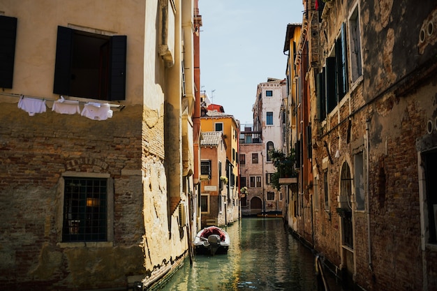 Canal avec des bateaux en face de maisons et blanchisserie accrochée à des cordes à linge entre les maisons sur le canal à Venise, Italie