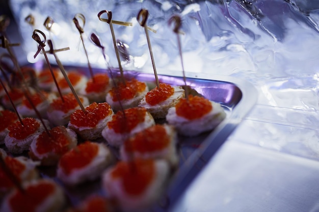 Canape au caviar rouge sur un plat en métal sur un grand bloc de glace avec des bougies sur fond d'ambiance festive avec éclairage au néon.