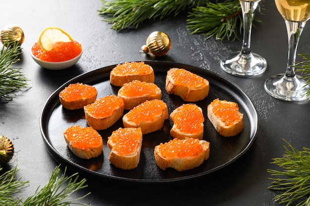 Canapé au caviar de saumon rouge pour le nouvel an ou la fête de Noël sur fond noir. Dîner de fêtes de fin d'année. Apéritif savoureux et champagne. Espace de copie.