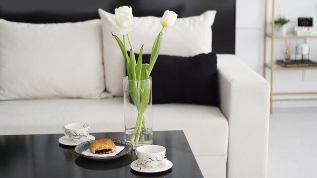 Canapé dans un intérieur moderne. Sur la table, un bouquet de tulipes, des tasses à café et un petit pain sucré