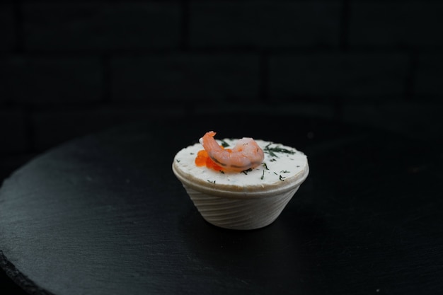 Un Canape Avec Du Pâté Et Des Crevettes Avec Des Verts Se Dresse Dans Une Assiette Blanche Sur Une Table Noire Dans Un Restaurant. Délicieuse Délicatesse De Fruits De Mer