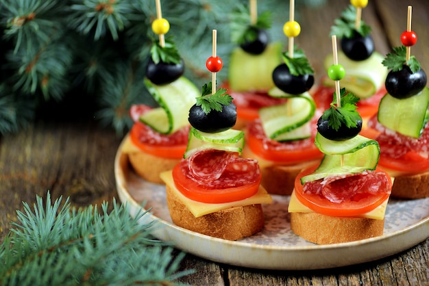 Canape de Noël sur brochette de pain baguette avec pain grillé, saucisse, tomate, concombre et olives.