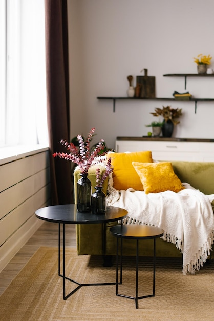 Un canapé vert avec des oreillers jaunes et une double table basse noire et une couverture dans un intérieur de salon de style scandinave moderne