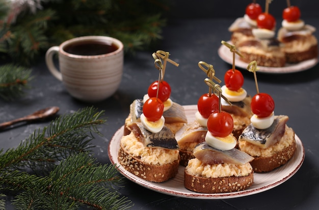 Canapés avec hareng salé, fromage, œufs de caille et tomates cerises sur croûtons de seigle et tasse de café sur table noire. Format horizontal. Fermer