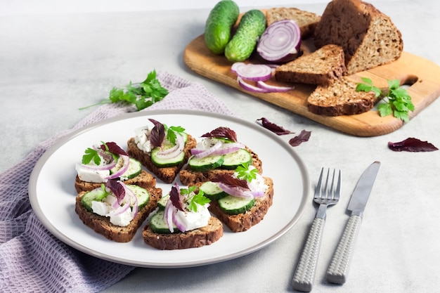 Canapés avec pain grillé aux graines de tournesol et de lin, fromage feta, concombre et oignon