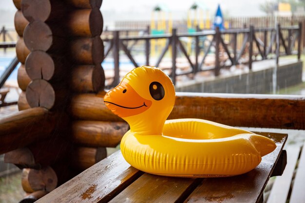 Un canard gonflable jaune se trouve sur une table en bois massive dans un belvédère confortable de l'une des maisons du centre de loisirs sur fond d'une grande piscine couverte de pluie battante