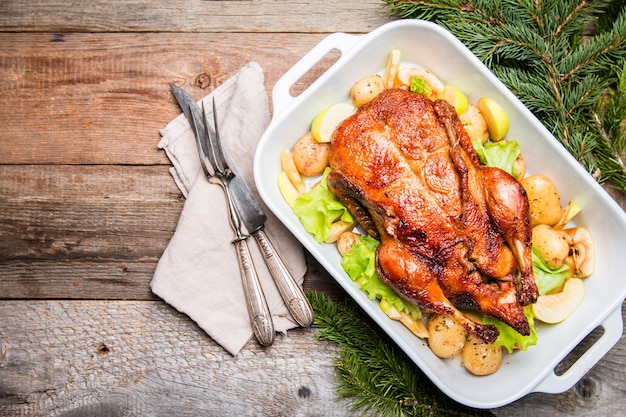 Canard de Noël avec des pommes et des herbes dans une casserole blanche sur une surface en bois, vue du dessus