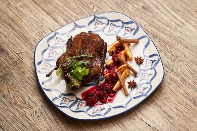 Canard rôti aux coings sur fond de table en bois. Canard entier cuit au four avec sauce aux coings et baies.