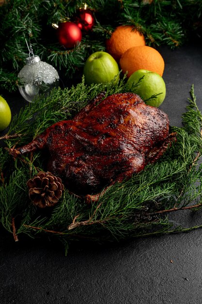 Canard rôti servi sur une assiette aux branchages verts et décoré de pommes de pin. Plat sur fond de Noël sombre