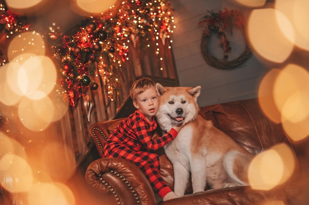 Candide authentique petit garçon heureux en pyjama à carreaux rouge câlins chien avec noeud papillon au lodge décoré de Noël