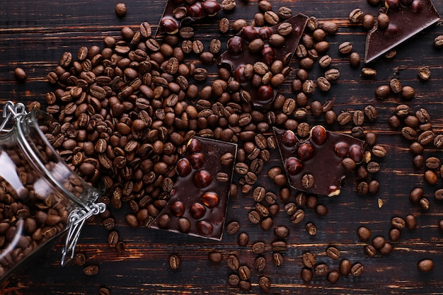 Une canette de café, des grains épars et du chocolat noir sur une table en bois.