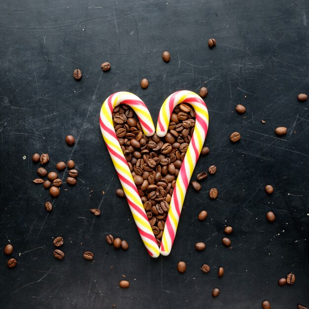 Canne de bonbons en forme de coeur avec vue de grains de café à plat sur fond noir