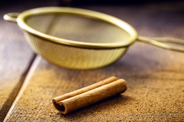 Cannelle en poudre et non pelée avec cuillère et tamis, saupoudrée sur la table, concept de cuisine saine.