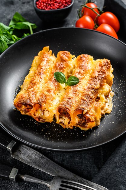 Cannelloni de pâtes italiennes maison avec boeuf et sauce tomate. Fond noir. vue de dessus