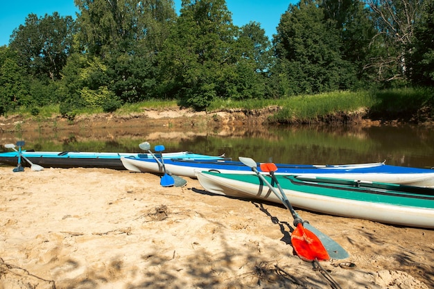 Des canoës touristiques avec pagaies se tiennent sur la côte de la rivière en été lors d'une randonnée aquatique Rafting sur des kayaks gonflables et à cadre double et triple voyage en famille aventure extrême en été