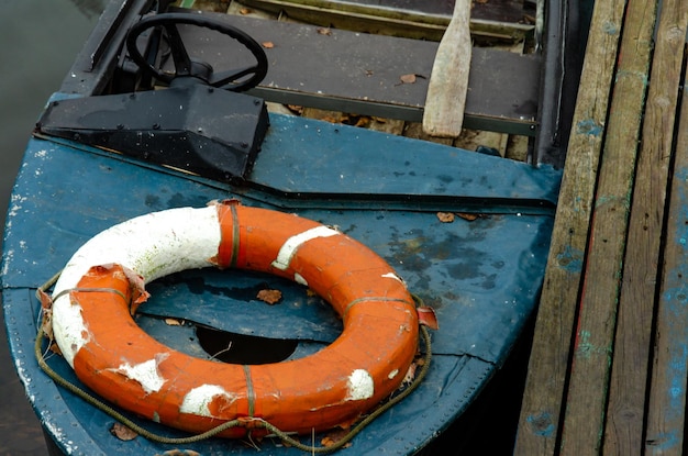 Un canot de sauvetage amarré près d'une jetée en bois À l'intérieur se trouve une rame en bois et un gilet de sauvetage Un vieux bateau à moteur avec un volant Mauvaises conditions de travail Utilisation de vieux équipements