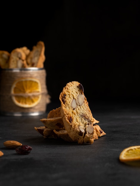 Cantucci (biscuits italiens cuits au four, biscotti) avec zeste d'orange, noix d'amande et canneberge séchée sur une terrasse en bois, planche à découper. Fond sombre.