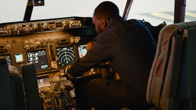 Capitaine afro-américain insérant les coordonnées de destination sur le panneau de commande et le tableau de bord dans le cockpit. Utilisation de la navigation pour piloter un avion avec boussole radar et interrupteur de moteur électrique.