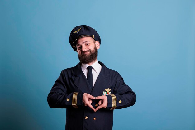 Capitaine d'avion heureux montrant le symbole d'amour en forme de coeur avec les doigts, geste romantique conceptuel. Aviateur d'avion de ligne amical en uniforme exprimant des sentiments d'affection vue de face plan moyen