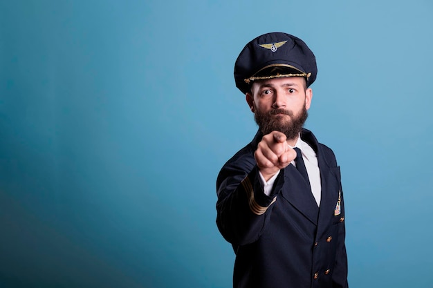 Capitaine d'avion sérieux pointant vers la caméra avec le doigt, recrutement de pilotes d'académie d'aviation. Aviateur confiant portant un uniforme professionnel et un portrait de vue de face de chapeau