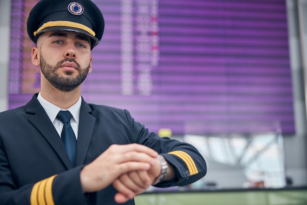 Capitaine de compagnie aérienne séduisante jeune homme en chapeau de pilote vérifiant l'heure avant le vol à l'aéroport