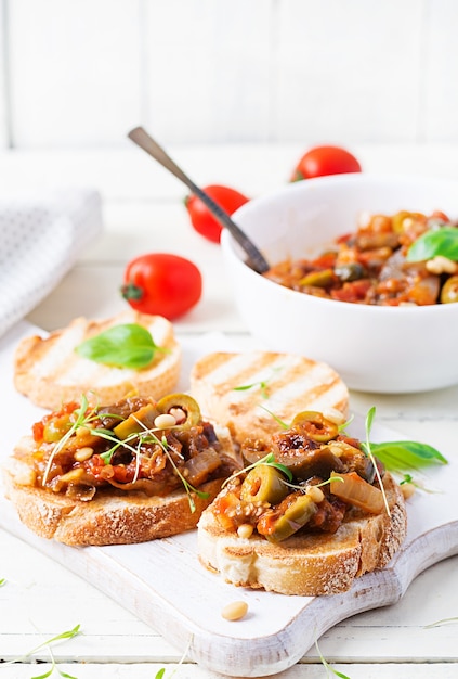 Caponata et pain grillé italiens traditionnels sur une table blanche en bois