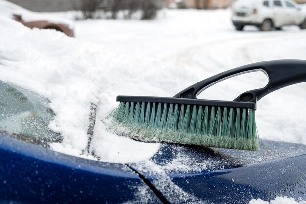 Le capot d'une voiture est nettoyé avec une brosse après une chute de neige