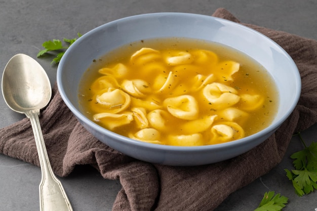 Cappelletti ou soupe tortellini brodo dans un bol avec assaisonnement sur fond de pierre