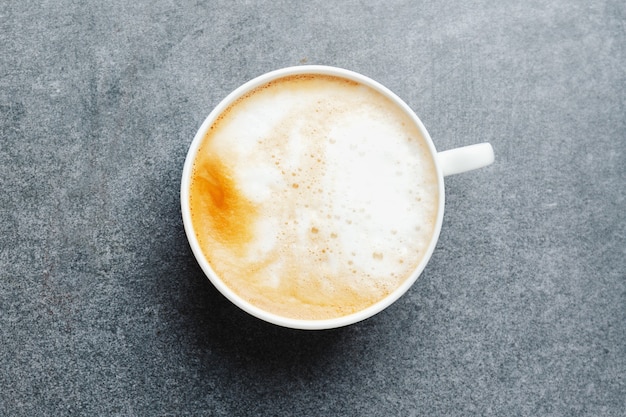 Cappuccino appétissant savoureux dans une tasse avec des haricots sur une table en béton.