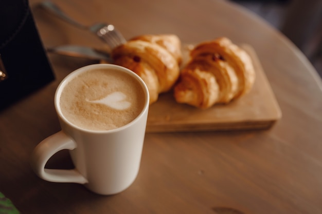 Cappuccino avec de beaux latte art et croissants sur une surface en bois