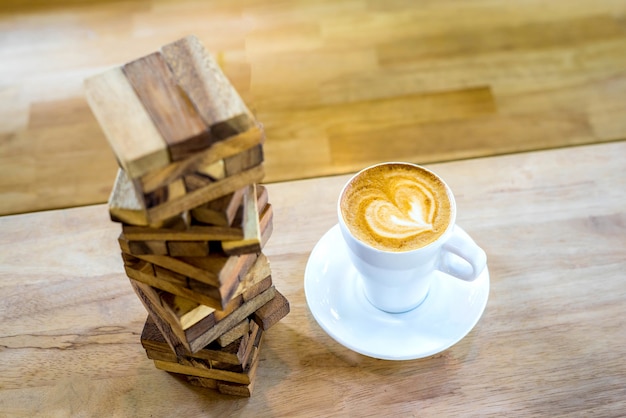 Cappuccino de café art chaud dans une tasse et Jenga jouet sur fond de table en bois