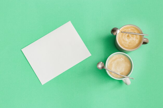 Cappuccino de café de deux tasses, petite cuillère et papier vierge pour écrire des idées. Temps de repos et de réflexion. Vue de dessus et mise à plat avec fond de menthe couleur tendance.