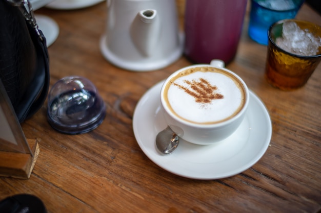 Cappuccino dans un pot en céramique blanche sur une table en bois, entourant une coupe en verre