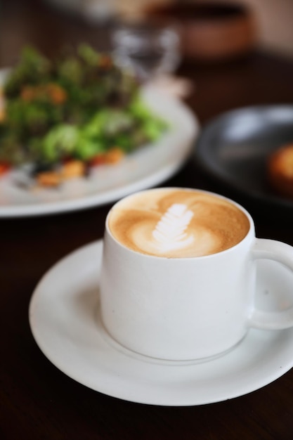 Photo cappuccino ou latte art café à base de lait sur la table en bois du café