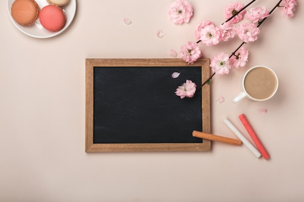Cappuccino tasse blanche avec des fleurs de sakura, macarons, tableau à craie sur un fond rose pastel