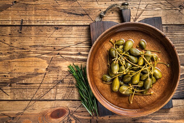 Câpres salées au vinaigre dans une assiette en bois. fond en bois. Vue de dessus. Espace de copie.