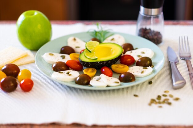 Caprese Salad. Un plat avec du fromage mozzarella et des tomates cerises, du poivre et des graines de citrouille. Un demi-avocat et une pomme verte pour compléter un repas végétarien sain