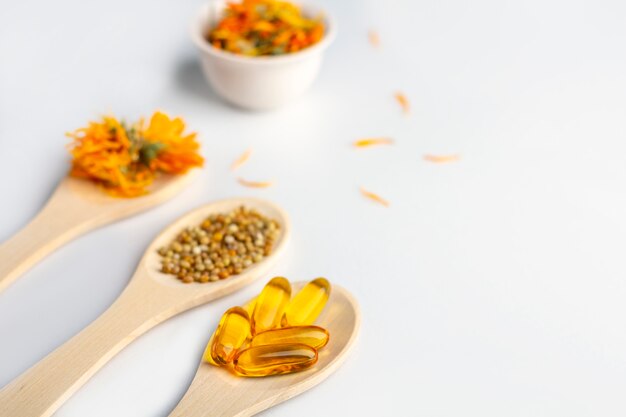 Capsule à base de plantes, vitamines naturelles, fleurs de calendula sec à la cuillère en bois sur fond blanc. Concept de soins de santé et de médecine alternative: homéopathie et naturopathie. Gros plan, espace copie