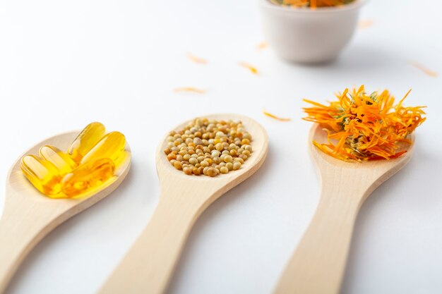 Capsule à base de plantes, vitamines naturelles, fleurs de calendula sec à la cuillère en bois sur fond blanc. Concept de soins de santé et de médecine alternative: homéopathie et naturopathie.