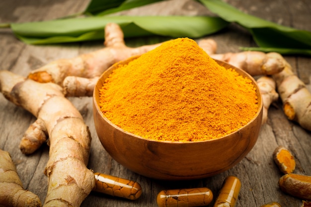 Capsule de curcuma et poudre de curcuma dans un bol en bois sur fond de table en bois ancien. Herbal